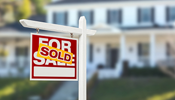 “Sold” sign in front of a suburban home.